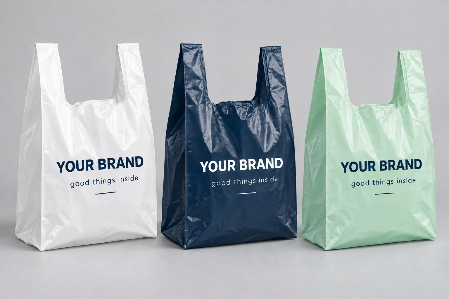 White, navy and mint traditional T-shirt plastic bags with one-piece integral handles and deep U-shaped openings. Illustrative product styling.
